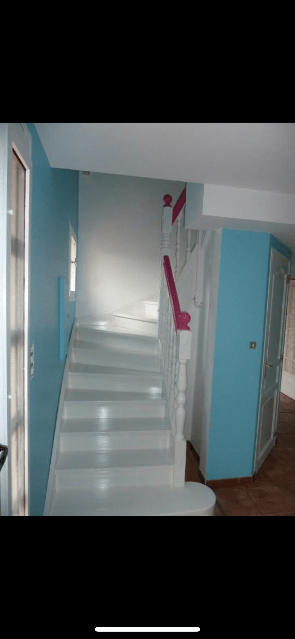 Escalier intérieur blanc brillant avec rampe fuchsia vif, murs bleu clair et balustres blancs. Ambiance moderne et lumineuse.