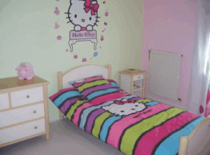 Chambre enfant colorée avec grand décalcomanie mural Hello Kitty. Lit simple à rayures multicolores Hello Kitty, commode et table de chevet en bois.