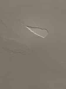 Mur texturé brun clair avec peinture écaillée, révélant une sous-couche blanche. Surface irrégulière et traces d'enduit.
