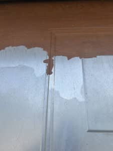 Une porte marron avec une peinture ou un revêtement écaillé sur la partie inférieure, révélant une surface grise rayée.