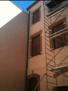 Façade rénovée d'un immeuble clair avec fenêtres à volets bois et encadrements en brique. Échafaudage de construction à droite.