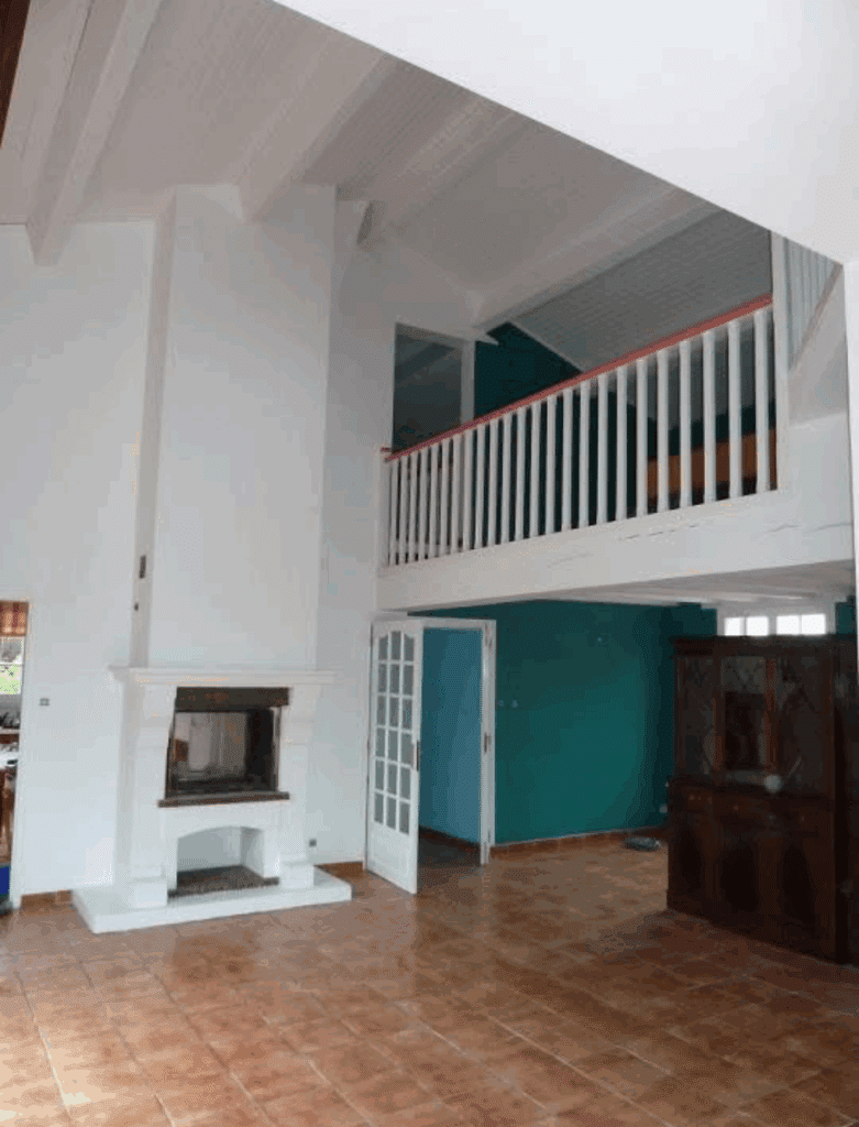 Salon lumineux avec mezzanine et cheminée – Ambiance moderne Salon spacieux avec cheminée blanche, carrelage marron, mezzanine à balustrade blanche et rose. Mur intérieur turquoise, plafond lambris.