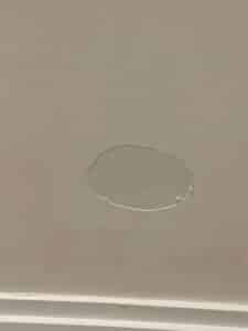 Mur beige clair avec un grand trou irrégulier, de forme ovale, révélant les couches internes. Une plinthe blanche est visible en bas.